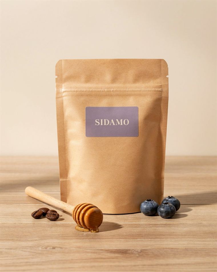 Äthiopien Sidamo: Kraftpapier-Tüte mit fliederfarbenem Etikett, daneben Blaubeeren und Honiglöffel